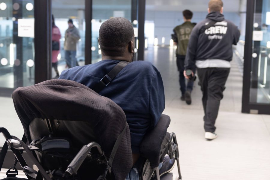 male wheelchair user going through automatic doors at Heathrow airport plus four people without mobility impairments on the concourse