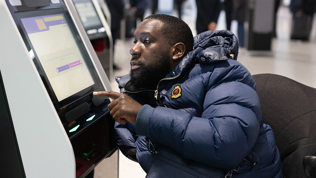 male wheelchair user is pressing buttons on a ticket screen at Heathrow airport