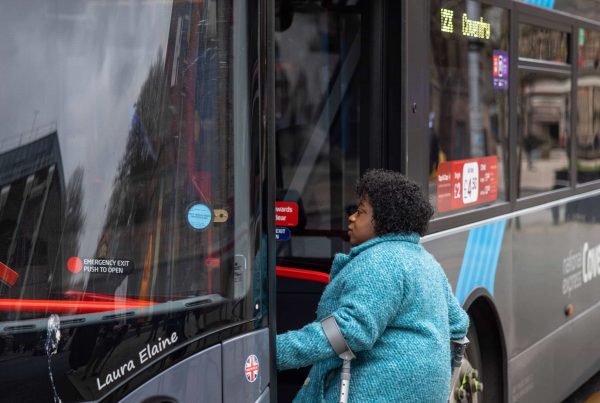 woman using mobility aids is boarding bus with one foot on the street and one on the bus